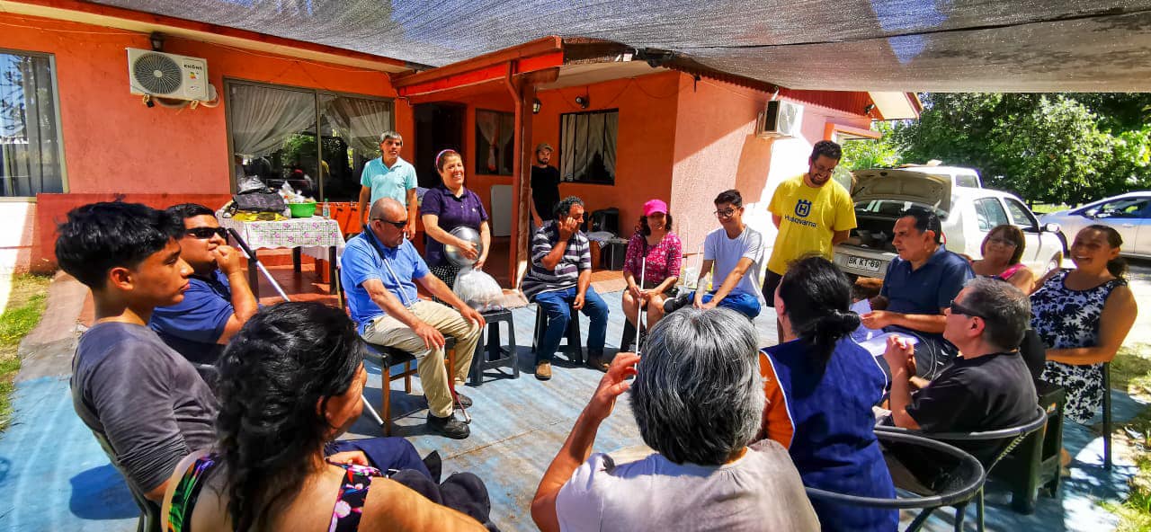 En el patio de una casa, un grupo de cerca de 20 personas están sentadas en círculo.