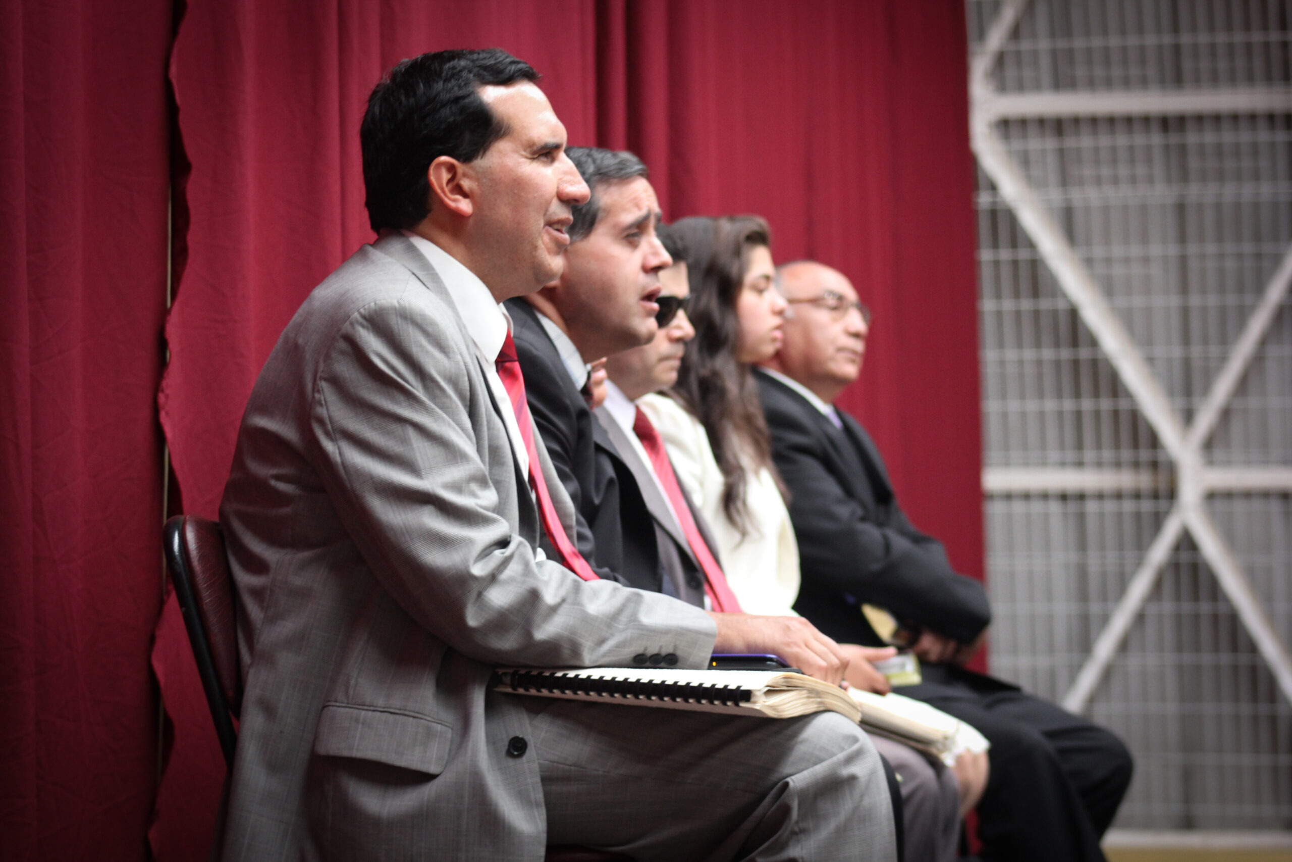 Cinco personas están sentadas en fila. El más próximo a la cámara sostiene un libro en Braille en sus muslos.